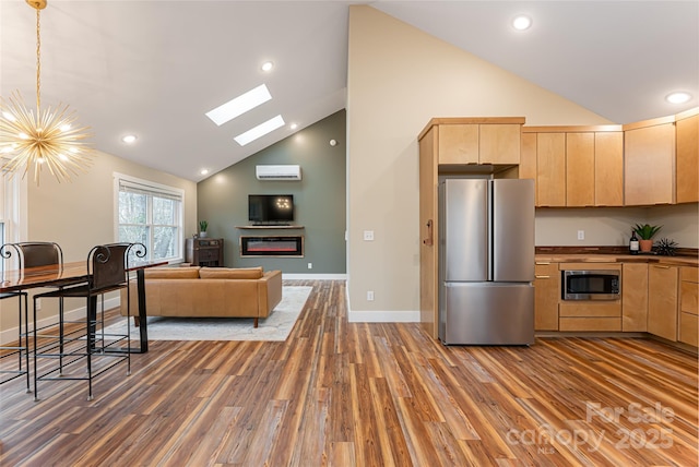 kitchen with wood finished floors, light brown cabinets, an AC wall unit, appliances with stainless steel finishes, and a glass covered fireplace