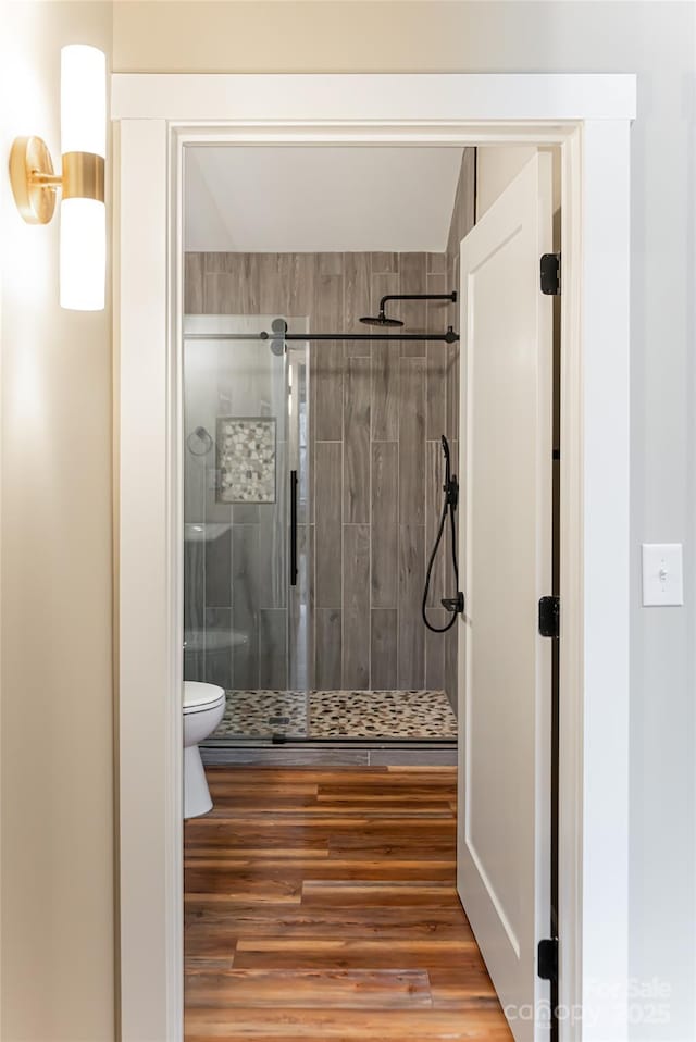 bathroom featuring toilet, wood finished floors, and a stall shower