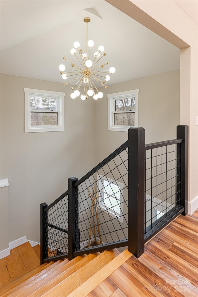 staircase featuring wood finished floors, baseboards, and a chandelier