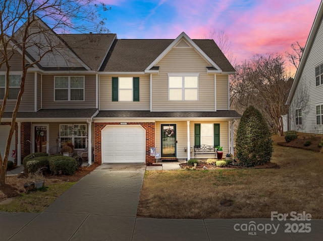 view of property with brick siding, a porch, roof with shingles, a yard, and driveway