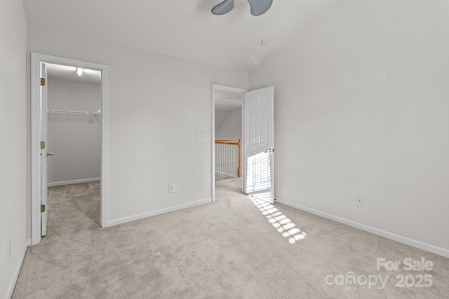 unfurnished bedroom with a walk in closet, baseboards, carpet, and vaulted ceiling