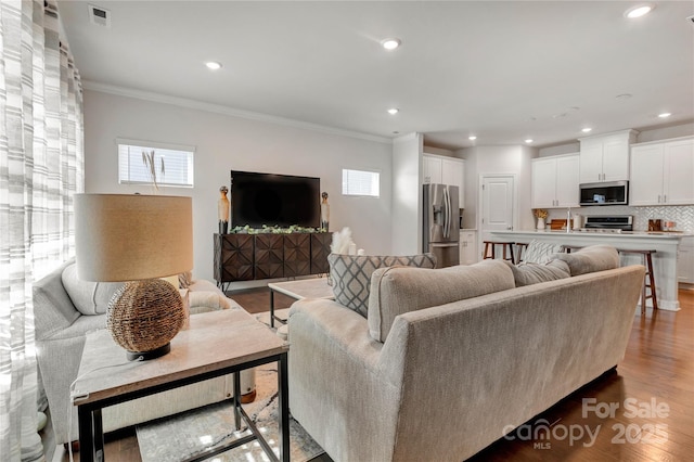 living room with a wealth of natural light, crown molding, visible vents, and wood finished floors