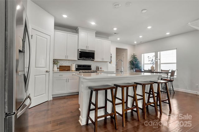 kitchen with stainless steel appliances, dark wood-type flooring, a center island with sink, and decorative backsplash