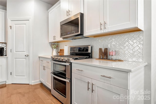 kitchen with tasteful backsplash, light wood-style flooring, light stone counters, stainless steel appliances, and white cabinetry