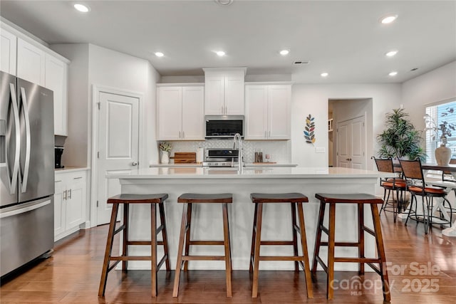 kitchen featuring stainless steel appliances, wood finished floors, backsplash, and light countertops