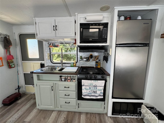 kitchen with black microwave, white cabinets, light wood-style floors, freestanding refrigerator, and tasteful backsplash