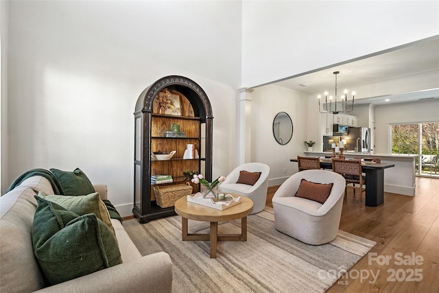 living area featuring baseboards, light wood finished floors, a high ceiling, decorative columns, and a notable chandelier