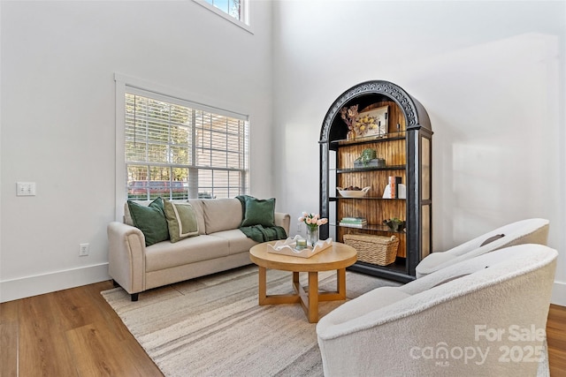 living area with a towering ceiling, baseboards, and wood finished floors