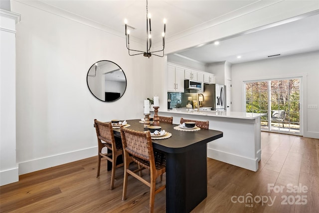 dining space featuring baseboards, wood finished floors, crown molding, a notable chandelier, and recessed lighting