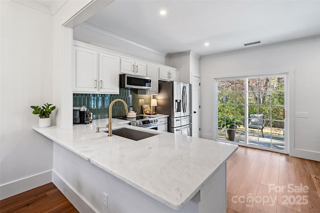 kitchen with tasteful backsplash, appliances with stainless steel finishes, white cabinetry, a sink, and wood finished floors