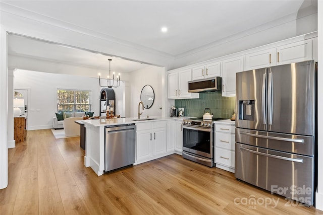 kitchen featuring appliances with stainless steel finishes, white cabinets, a sink, and a peninsula