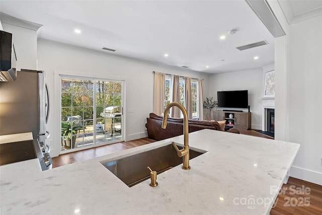 kitchen with wood finished floors, a sink, visible vents, freestanding refrigerator, and light stone countertops