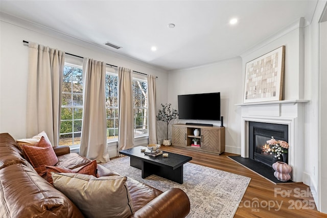 living room with recessed lighting, a fireplace with flush hearth, wood finished floors, visible vents, and crown molding