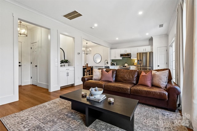 living room with a chandelier, wood finished floors, visible vents, baseboards, and crown molding