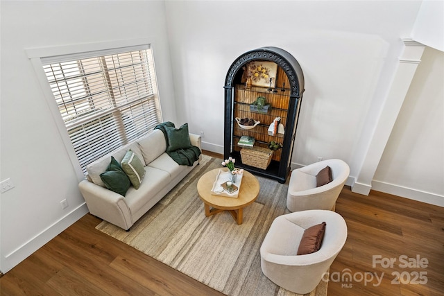 living area with baseboards, wood finished floors, and ornate columns