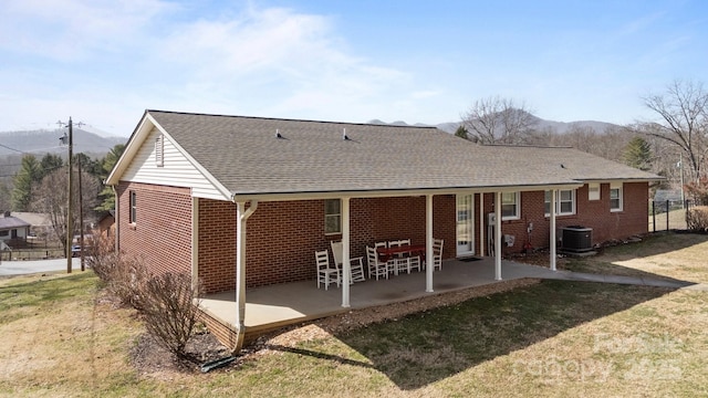 back of property with brick siding, central air condition unit, a shingled roof, a lawn, and a patio area