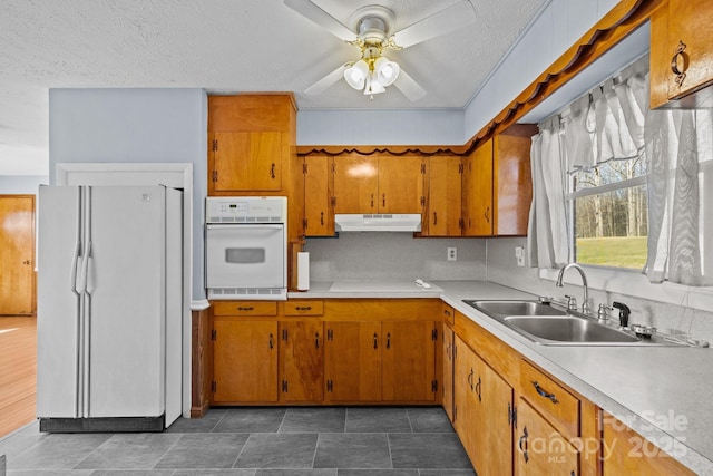 kitchen featuring white appliances, brown cabinets, a sink, and under cabinet range hood