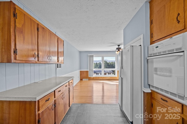 kitchen with white appliances, brown cabinets, and a wainscoted wall