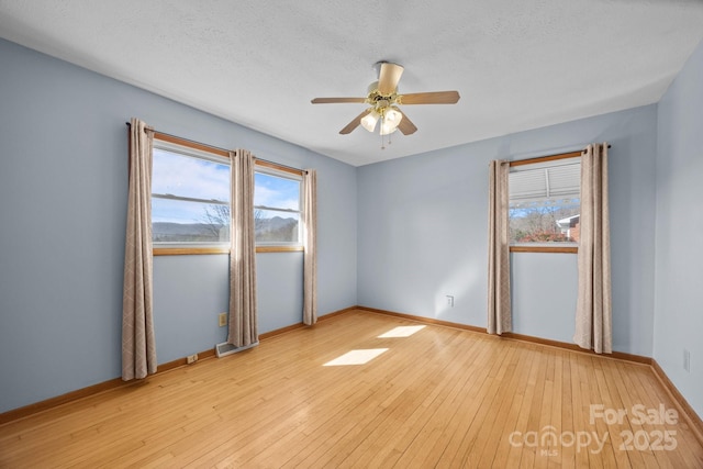 empty room featuring ceiling fan, light wood finished floors, and a wealth of natural light