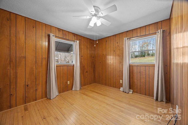 empty room featuring light wood-type flooring, a healthy amount of sunlight, a ceiling fan, and wood walls