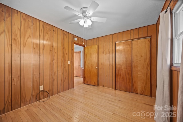 unfurnished bedroom featuring a closet, wood-type flooring, a ceiling fan, and wooden walls