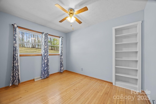 spare room with baseboards, visible vents, wood-type flooring, a textured ceiling, and built in shelves