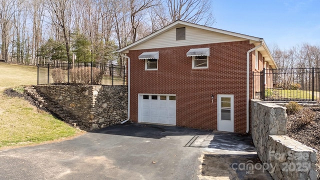 view of side of property with a garage, brick siding, fence, and aphalt driveway