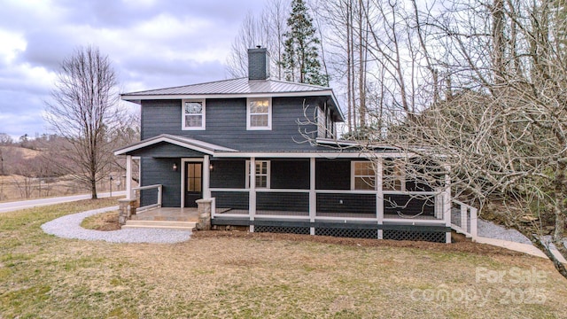 back of property featuring a chimney, metal roof, and a yard