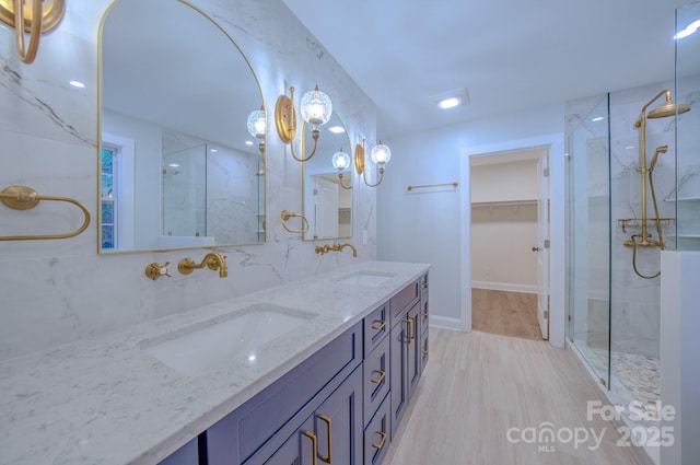 bathroom featuring double vanity, a marble finish shower, a sink, and wood finished floors