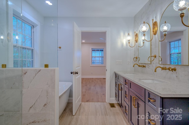 bathroom featuring a freestanding bath, double vanity, a sink, and baseboards