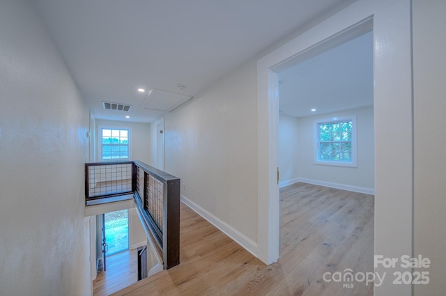 hall with attic access, visible vents, baseboards, and wood finished floors