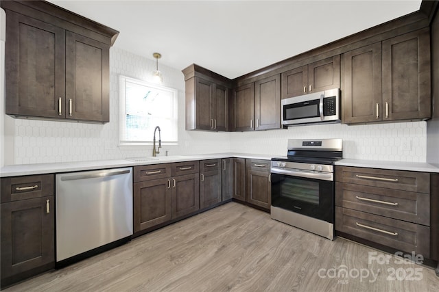 kitchen with dark brown cabinetry, appliances with stainless steel finishes, light countertops, light wood-type flooring, and a sink