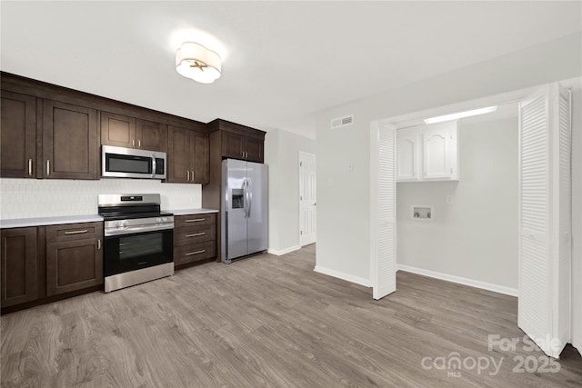 kitchen featuring stainless steel appliances, visible vents, dark brown cabinetry, and light wood-style flooring