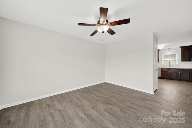 spare room featuring a sink, a ceiling fan, baseboards, and wood finished floors