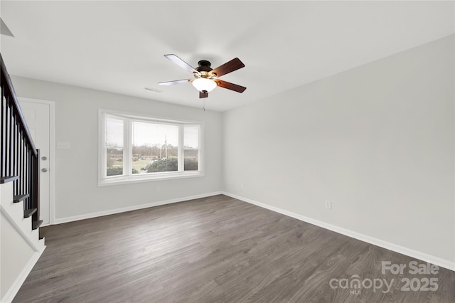 unfurnished room with dark wood-style flooring, a ceiling fan, visible vents, baseboards, and stairway