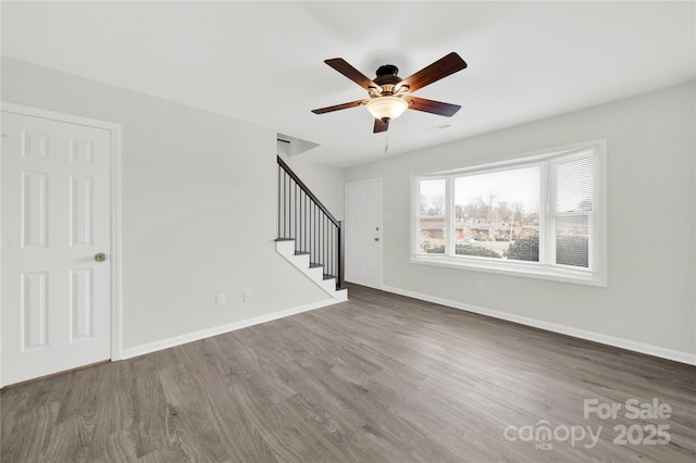 unfurnished room featuring a ceiling fan, baseboards, stairway, and wood finished floors