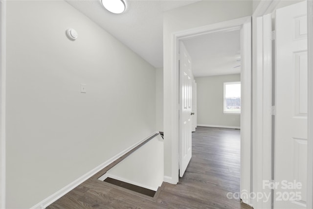 hallway featuring baseboards, wood finished floors, and an upstairs landing