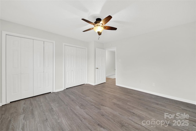 unfurnished bedroom featuring baseboards, ceiling fan, wood finished floors, and multiple closets