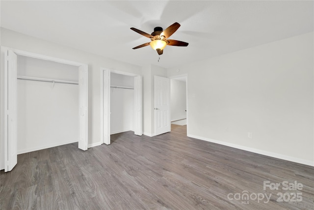 unfurnished bedroom featuring ceiling fan, baseboards, multiple closets, and wood finished floors