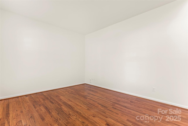 spare room with baseboards and wood finished floors