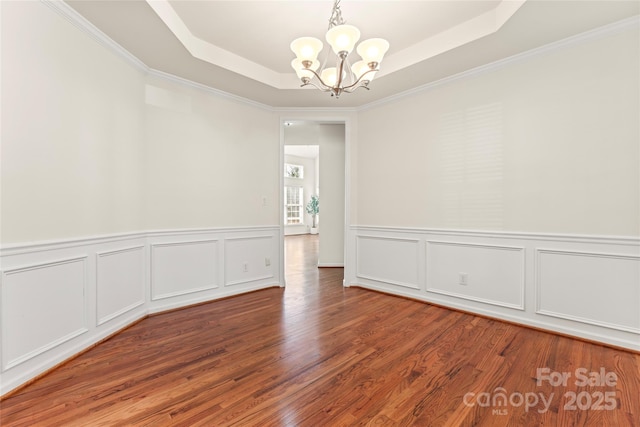 empty room featuring an inviting chandelier, crown molding, a raised ceiling, and wood finished floors