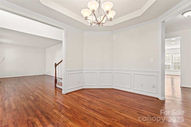 spare room with a chandelier, a raised ceiling, stairway, and wood finished floors