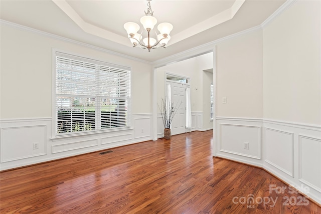 unfurnished room with visible vents, a raised ceiling, ornamental molding, wood finished floors, and a notable chandelier