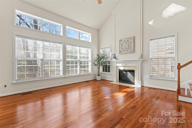 unfurnished living room featuring high vaulted ceiling, a premium fireplace, wood finished floors, visible vents, and stairs