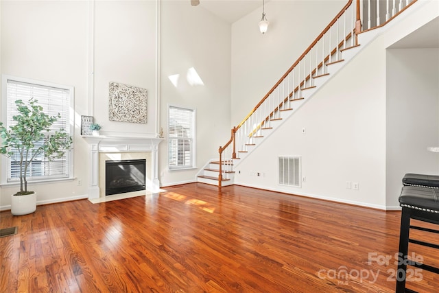 unfurnished living room with a fireplace, wood finished floors, a towering ceiling, visible vents, and stairway