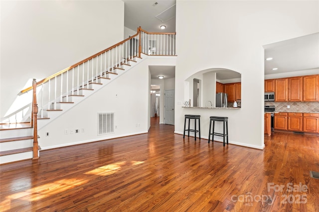 unfurnished living room featuring baseboards, visible vents, stairway, dark wood-type flooring, and a high ceiling