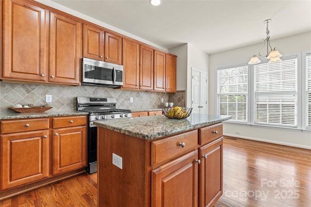 kitchen with appliances with stainless steel finishes, brown cabinets, dark wood-style floors, tasteful backsplash, and dark stone countertops