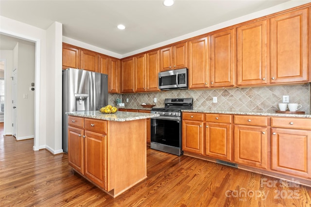 kitchen with stainless steel appliances, dark wood-type flooring, a kitchen island, and light stone countertops