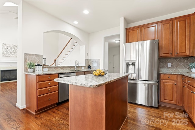 kitchen with a center island, dark wood-style flooring, stainless steel appliances, a sink, and light stone countertops