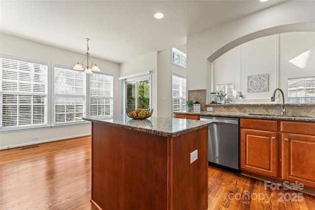 kitchen with visible vents, a kitchen island, dark wood-style flooring, stainless steel dishwasher, and a sink